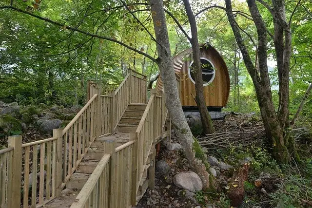 A glamping pod in the woods, with a wooden bridge in the foreground