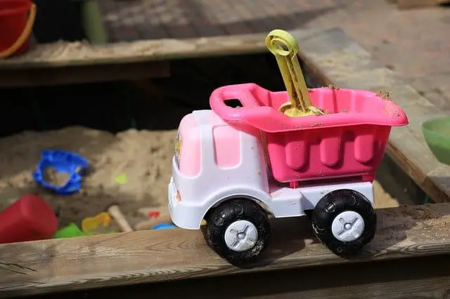 Sand toys in a sandbox, including a pink digger truck
